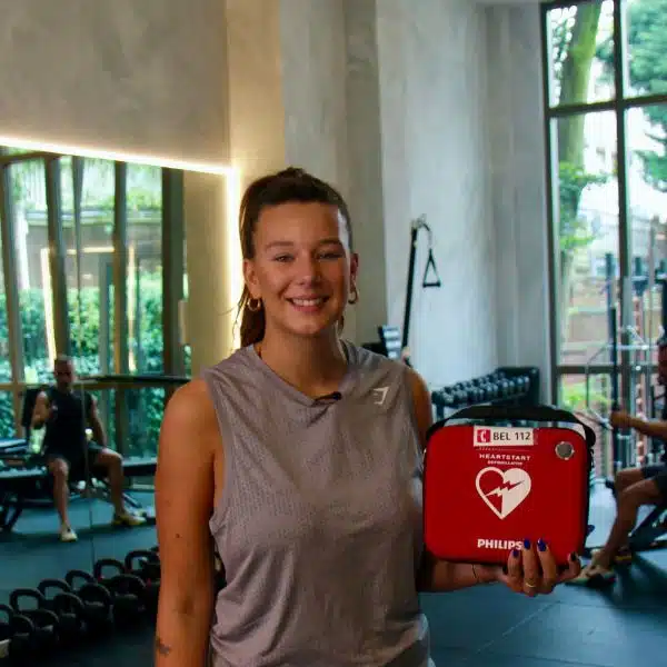 Frau hält roten Defibrillatorkoffer im Fitnessstudio